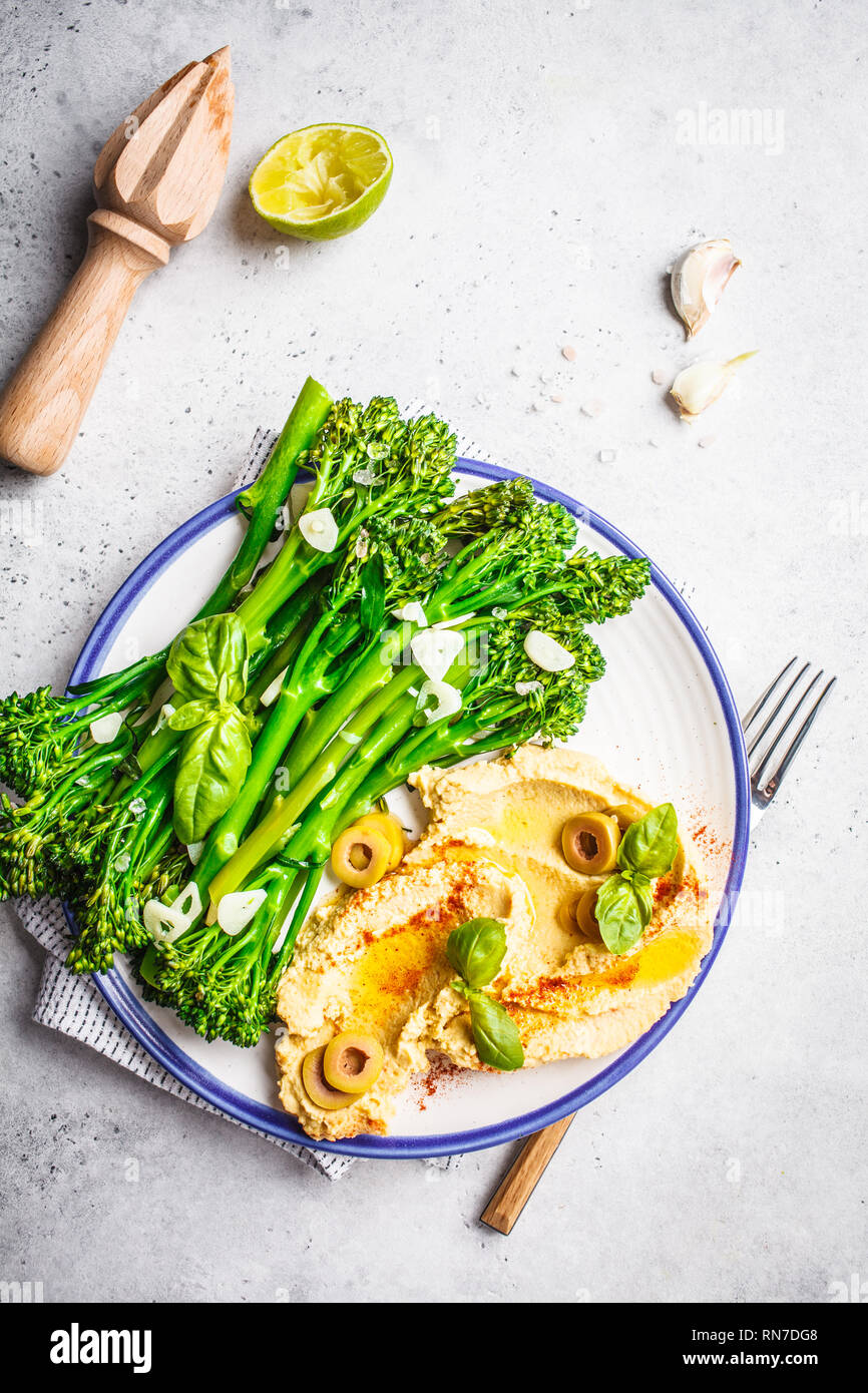 Broccolini cotti con hummus su una piastra bianca, vista dall'alto. Sano cibo vegan concetto. Foto Stock