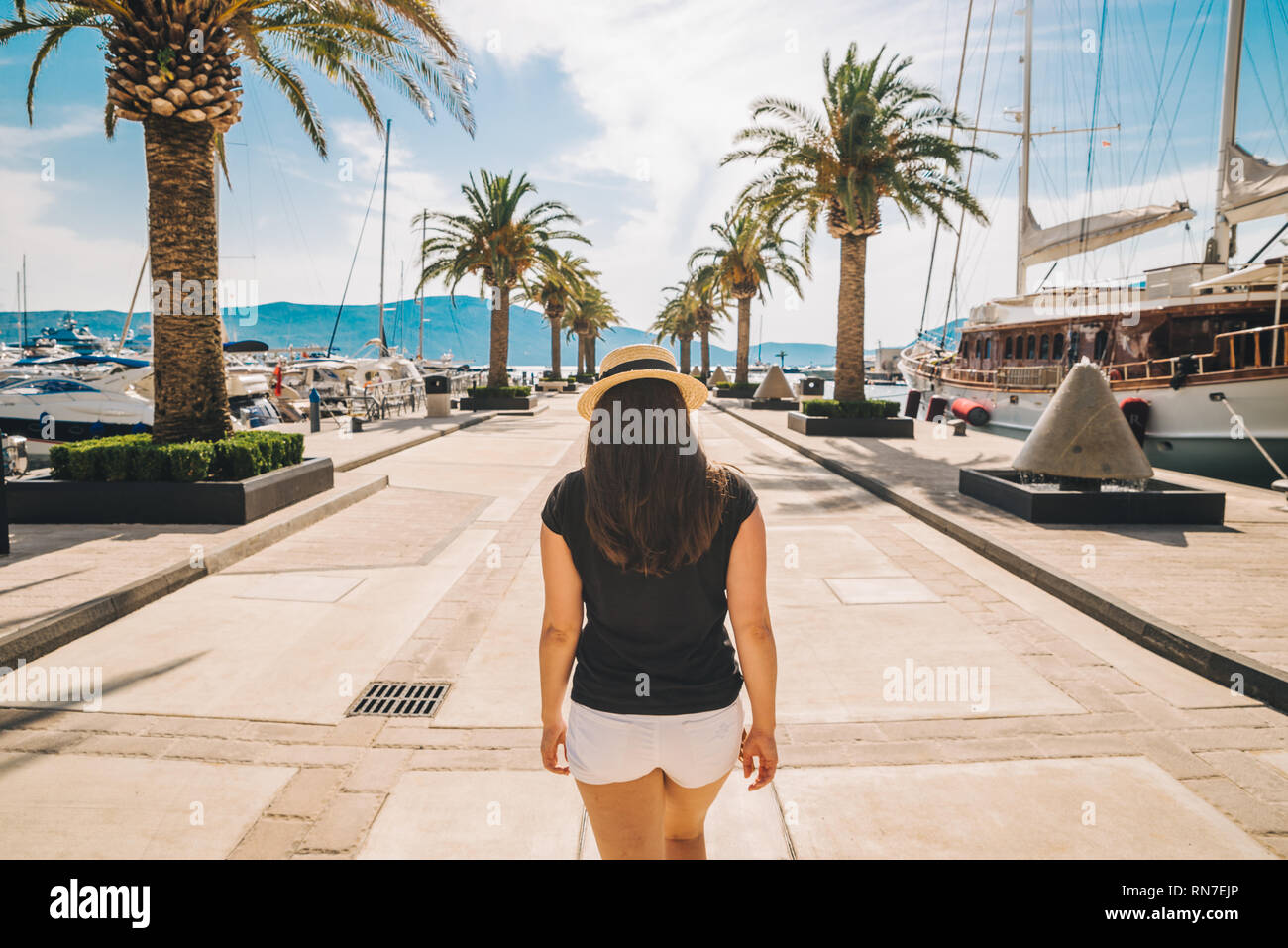 La donna a piedi dal molo di sole con palme. montagne e yachts sullo sfondo Foto Stock