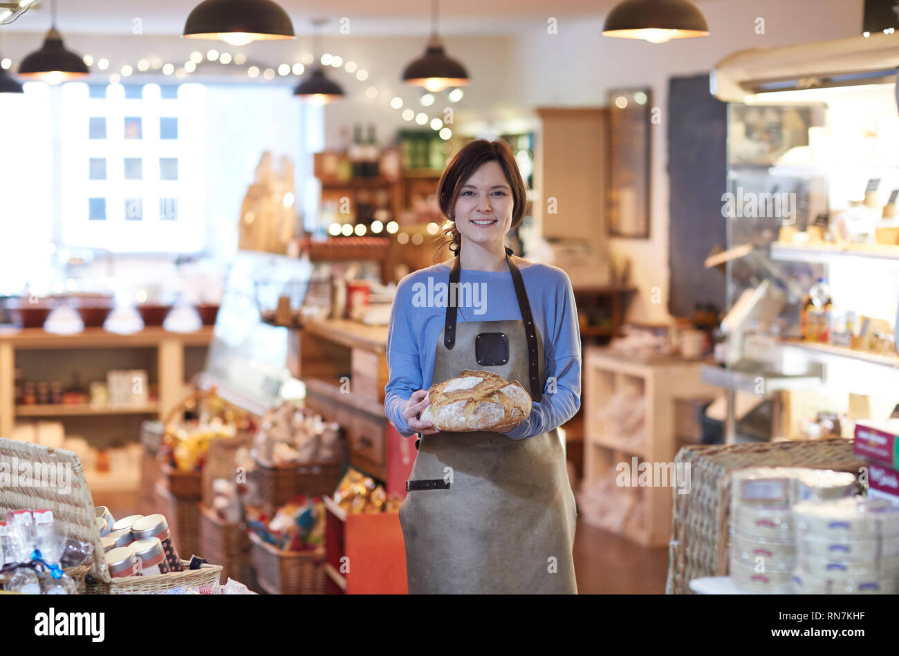 Ritratto Di Donna sorridente Proprietario del negozio delicatessen indossando grembiuli azienda pagnotta di pane Foto Stock