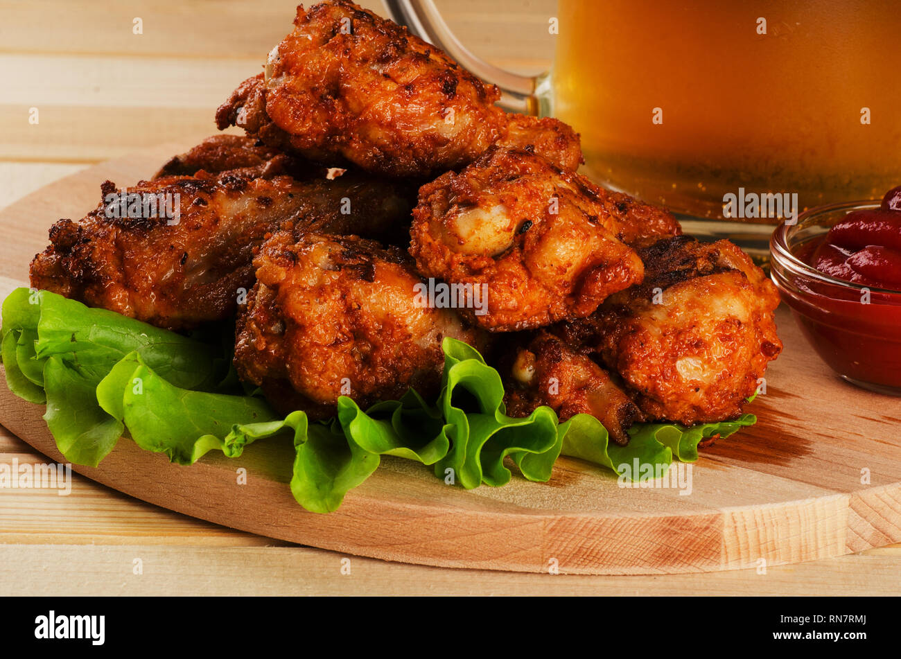 Le ali di pollo croccanti impanati con sause e birra su di un tagliere Foto Stock