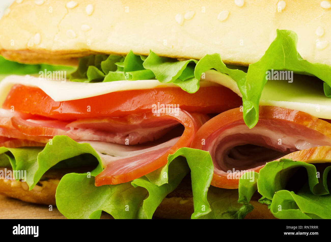 Close-up foto di una fresca baguette croccanti deli sandwich. Sandwich di soddisfare, pancetta, insalata di verdure, lattuga, pomodoro, su un fresco tagliato a fette di pane di segale Foto Stock