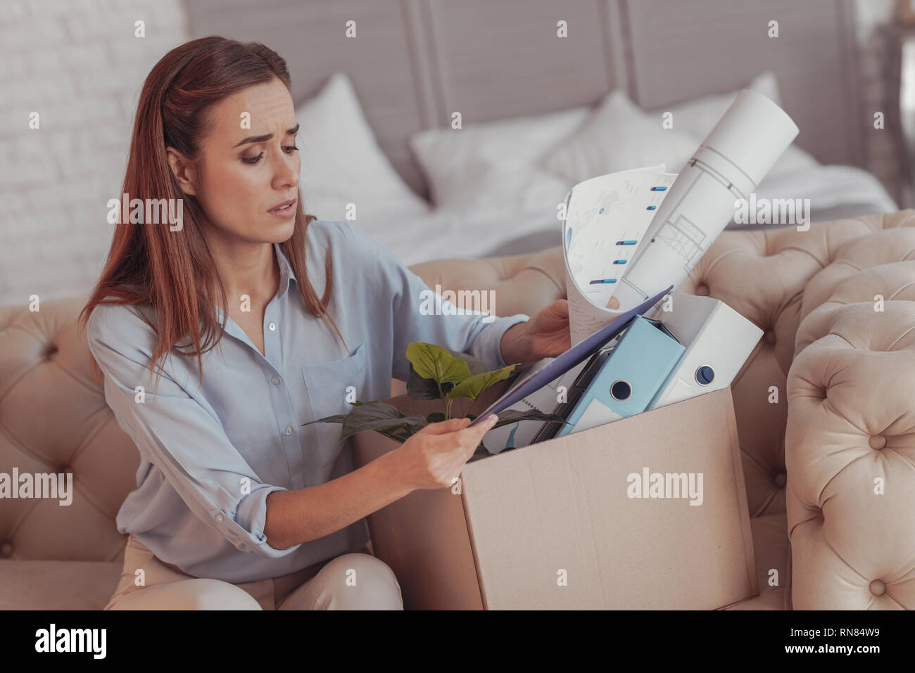 Nessun job. Vita della giovane donna invecchiato con il dolore nel suo sguardo seduti sul divano e lo smistamento del suo ufficio stuff Foto Stock