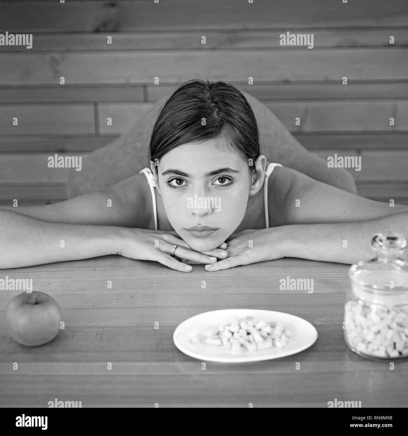 Cercando di fare una scelta giusta. Donna graziosa occhiata a Apple e marshmallows. Donna di scegliere quale tipo di cibo da mangiare. Biologici e naturali o dolce e malsano Foto Stock