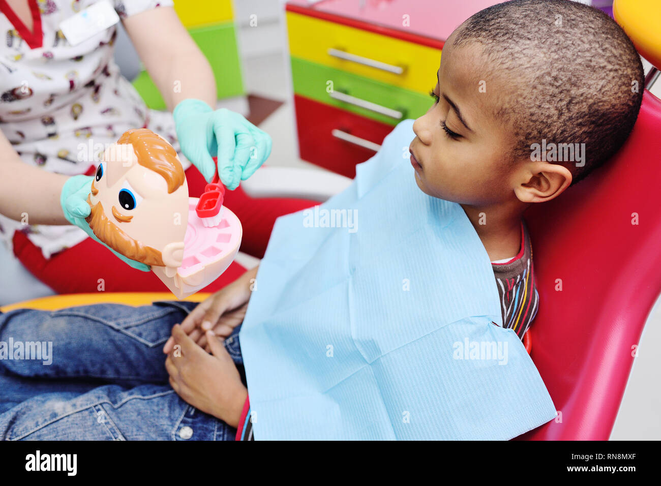 Un Dentista pediatrico insegna un americano africano bambino che siede in una poltrona odontoiatrica per spazzolare i denti correttamente. Foto Stock