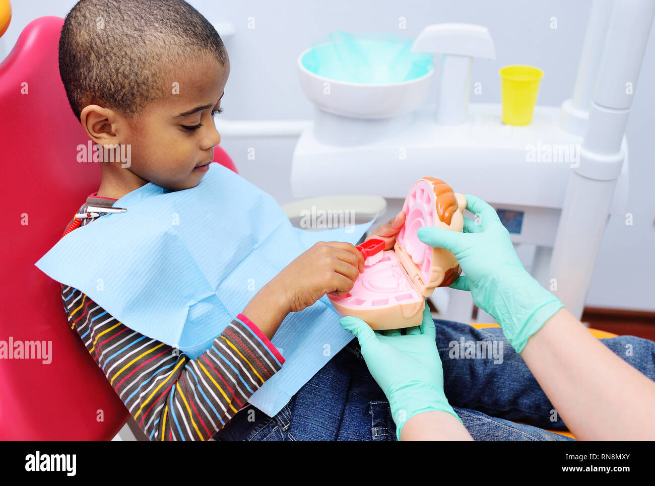 Un Dentista pediatrico insegna un americano africano bambino che siede in una poltrona odontoiatrica per spazzolare i denti correttamente. Foto Stock