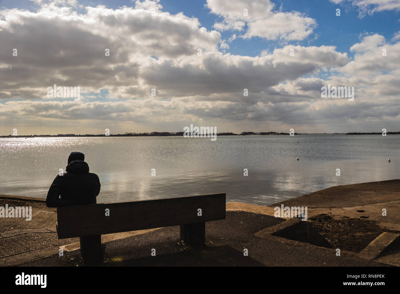 Uomo su una panchina in cerca di un mare calmo Foto Stock