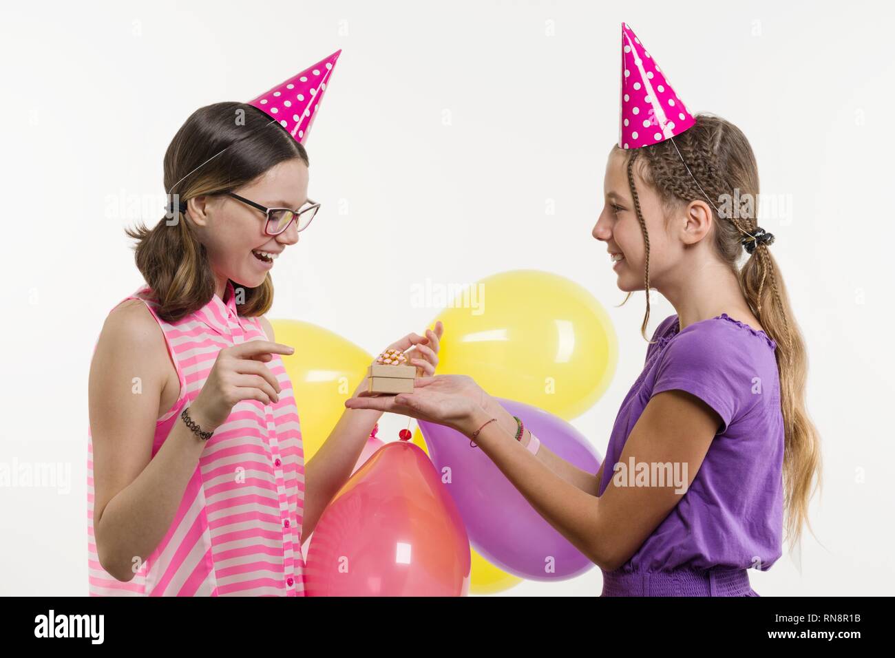 Festa di compleanno. Le ragazze adolescenti dare un regalo. Sfondo bianco, in festosa cappelli con palloncini Foto Stock