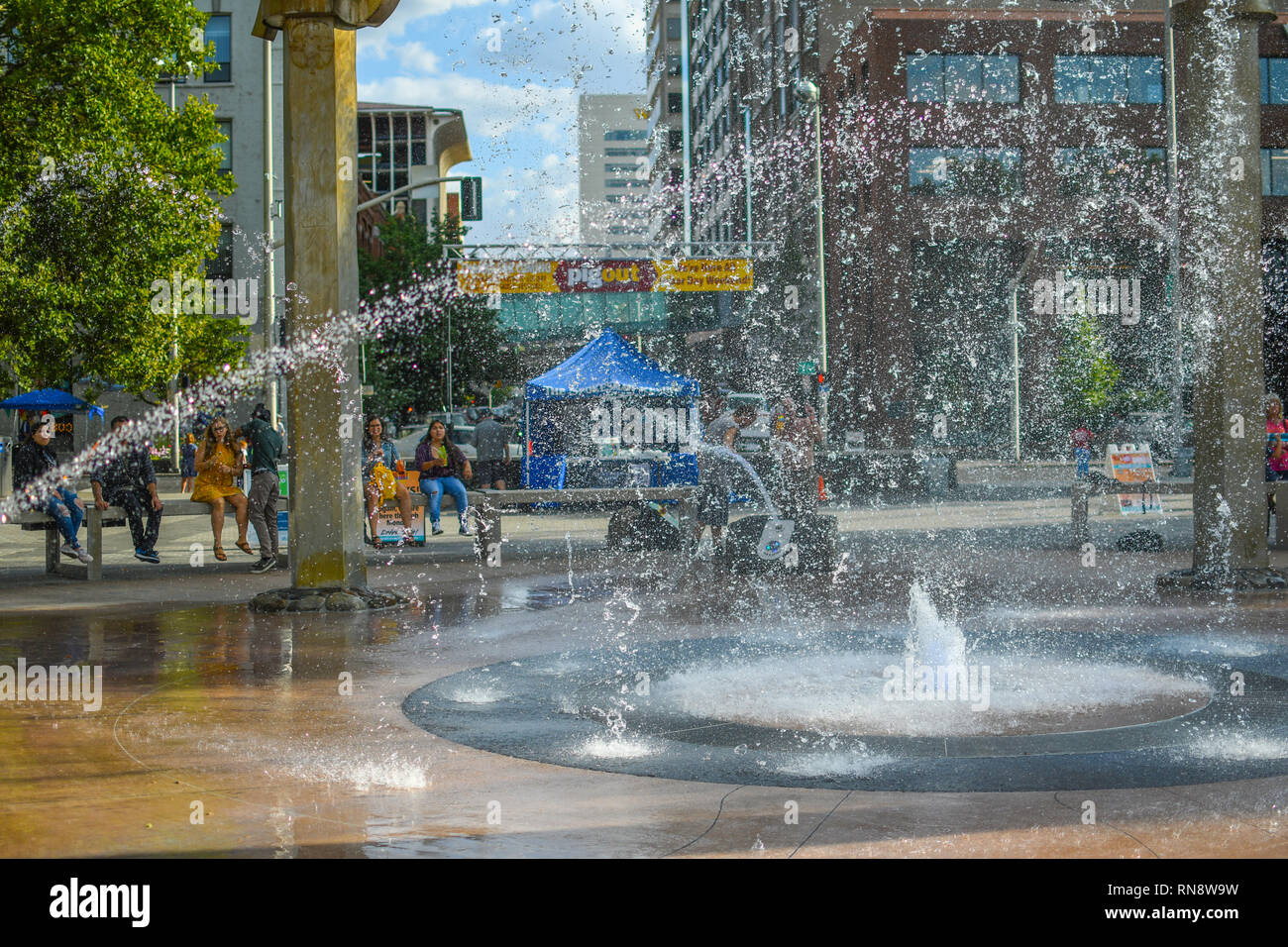 I turisti e i locali godono di un giorno di estate a Riverfront Park di Spokane, Washington, come essi siedono intorno alla fontana rotante e guardare lo spruzzo di acqua Foto Stock