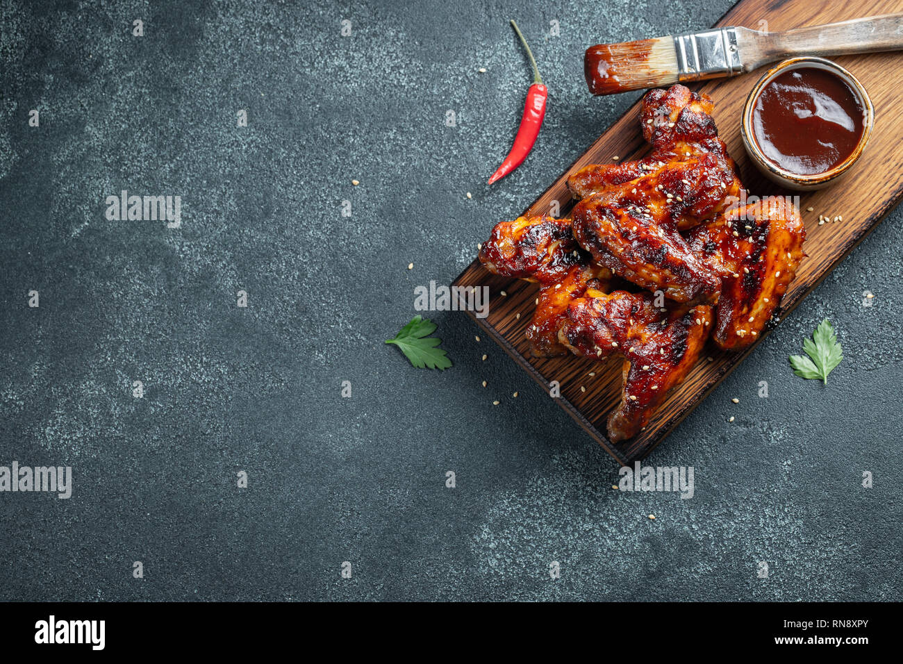 Arrosto di ali di pollo in salsa barbecue con semi di sesamo e prezzemolo su una tavola di legno su una tavola di calcestruzzo. Vista da sopra con copia spazio. Gustosi snack per Foto Stock