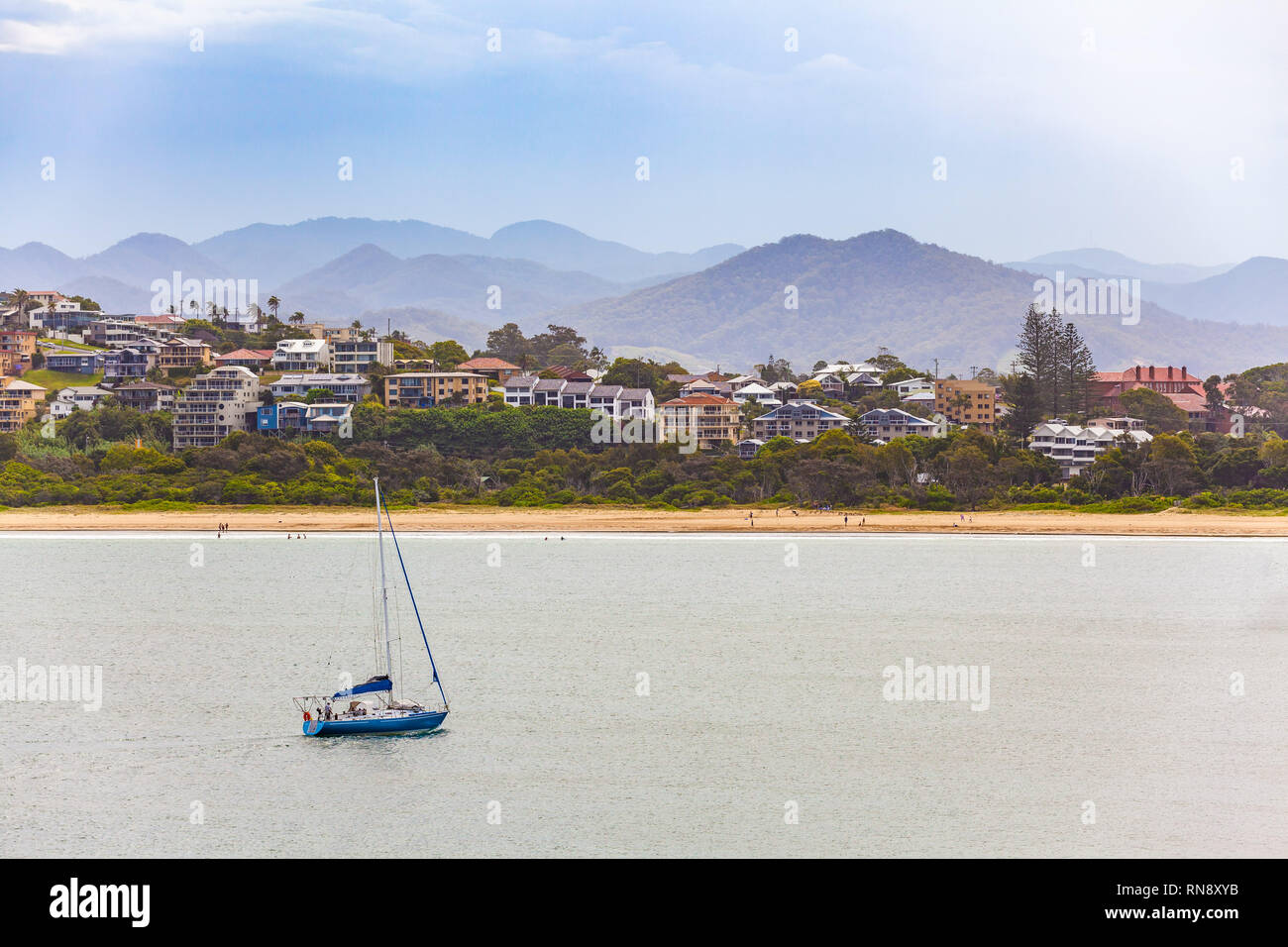 Barca a vela vela a Coffs Harbour con le case di lusso e le montagne sullo sfondo Foto Stock