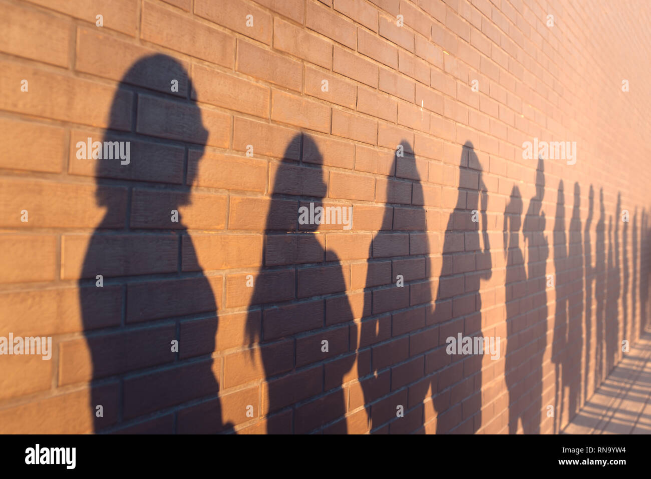 Una linea di ombre di persone schierate contro in rosso di un muro di mattoni. Stare in coda per le modifiche Foto Stock