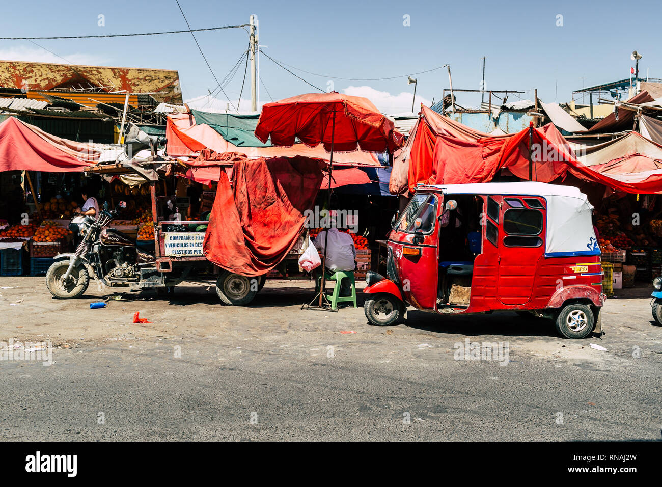 Un rosso tuktuk motociclo taxi e un altro autoveicolo parcheggiato dietro le bancarelle del mercato nel sud piccola cittadina americana di Ica, Perù. Foto Stock