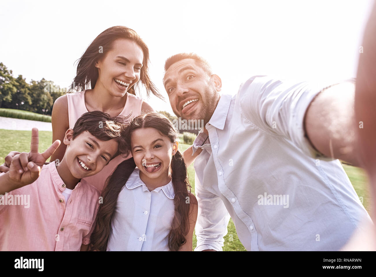 Bei ricordi. Famiglia di quattro tenendo selfie foto sullo smartphone nella luce del sole sorride felice close-up Foto Stock