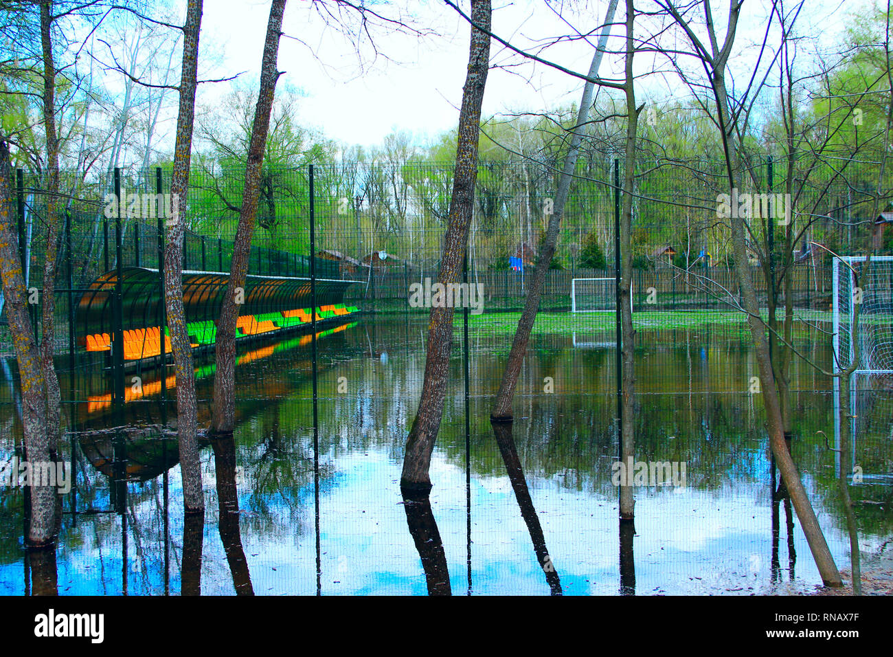 Campo di calcio durante la piena del fiume. Piccolo stadio di calcio recintato con net è allagato con acqua durante l'alluvione. Il calcio ha preso break Foto Stock