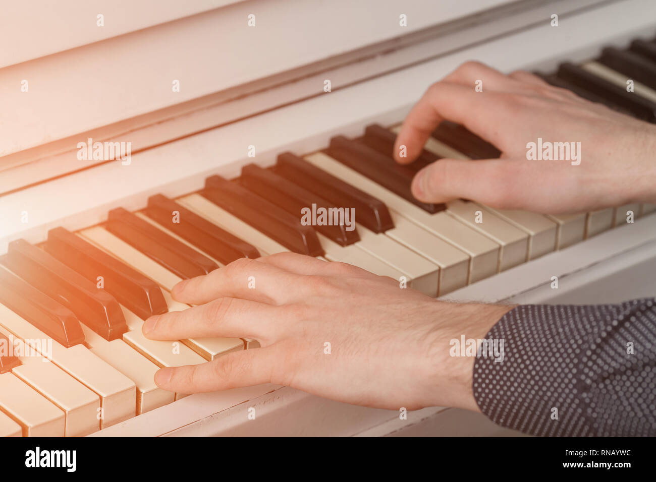 Gli uomini le mani sulla tastiera del pianoforte con la luce solare Foto Stock