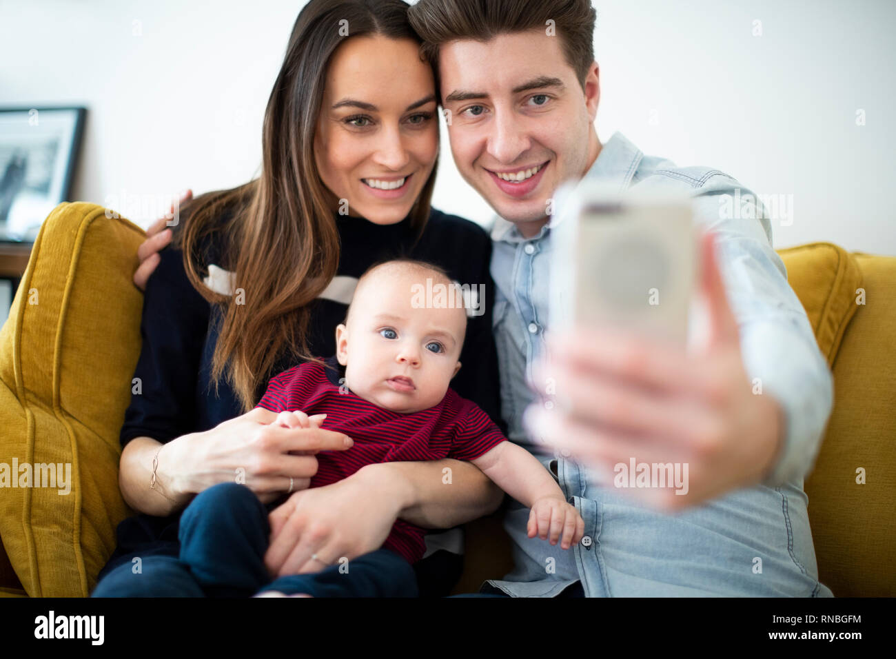 Famiglia seduti sul divano di casa in posa per Selfie sul telefono cellulare Foto Stock