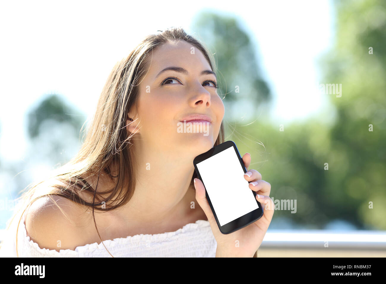 Malinconici ragazza che mostra a vuoto della fotocamera smart phone screen mockup in un parco Foto Stock