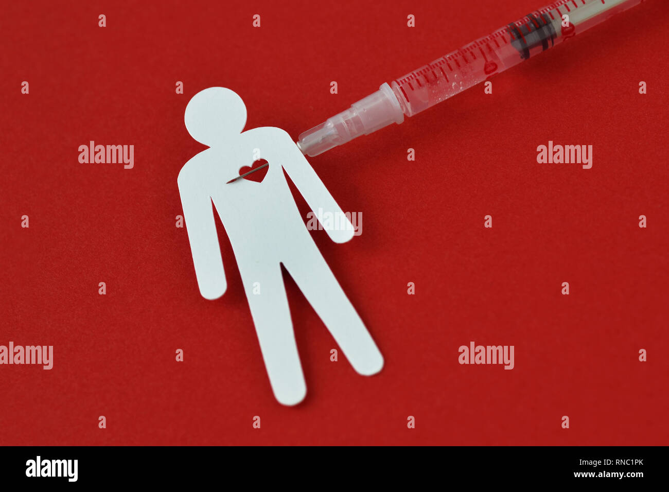 Uomo di carta con il cuore e con la siringa su sfondo rosso - Nozione di tossicodipendenza. Foto Stock
