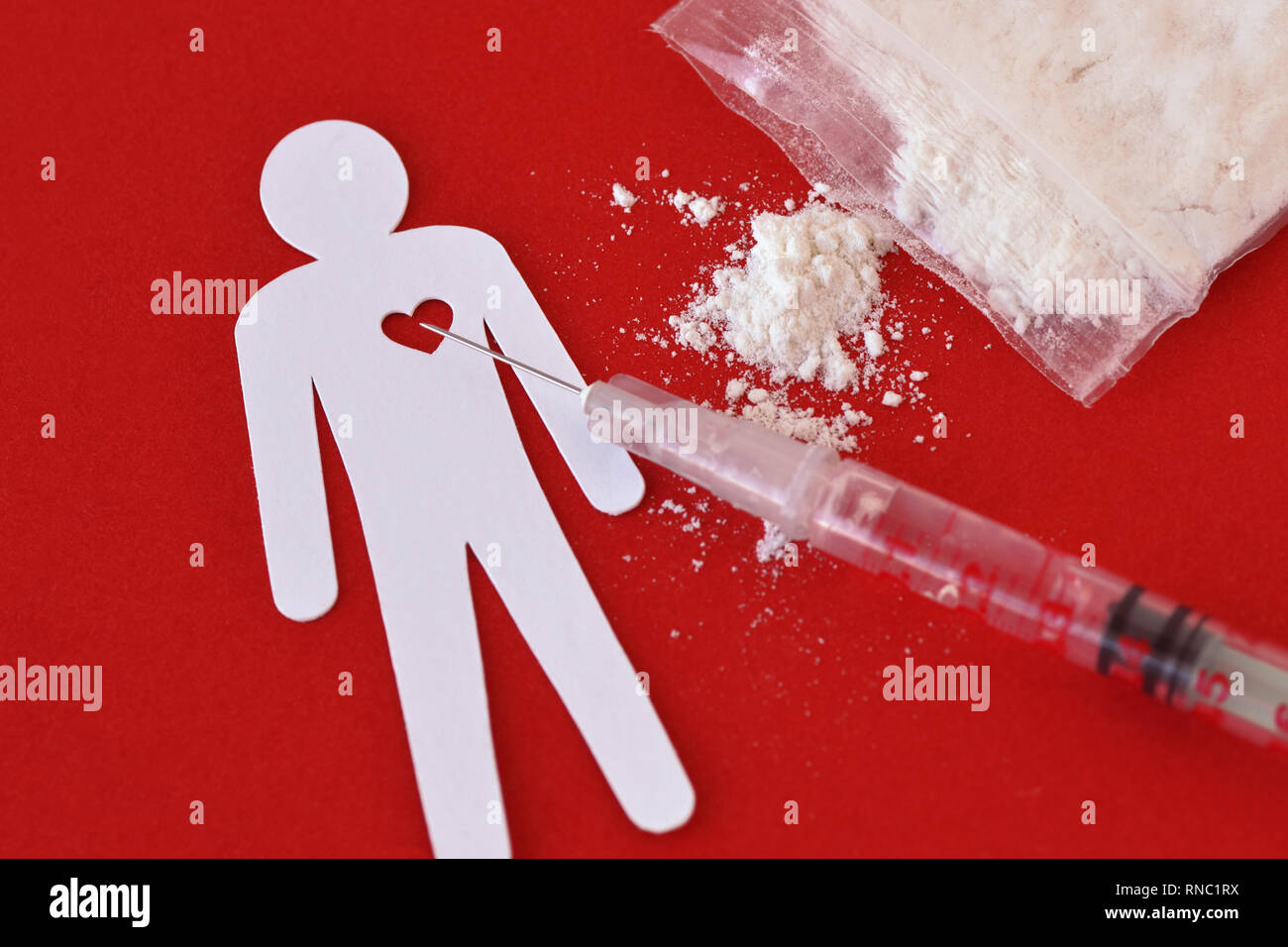 Uomo di carta con il cuore, la siringa e la bustina di droga su sfondo rosso - Nozione di tossicodipendenza. Foto Stock