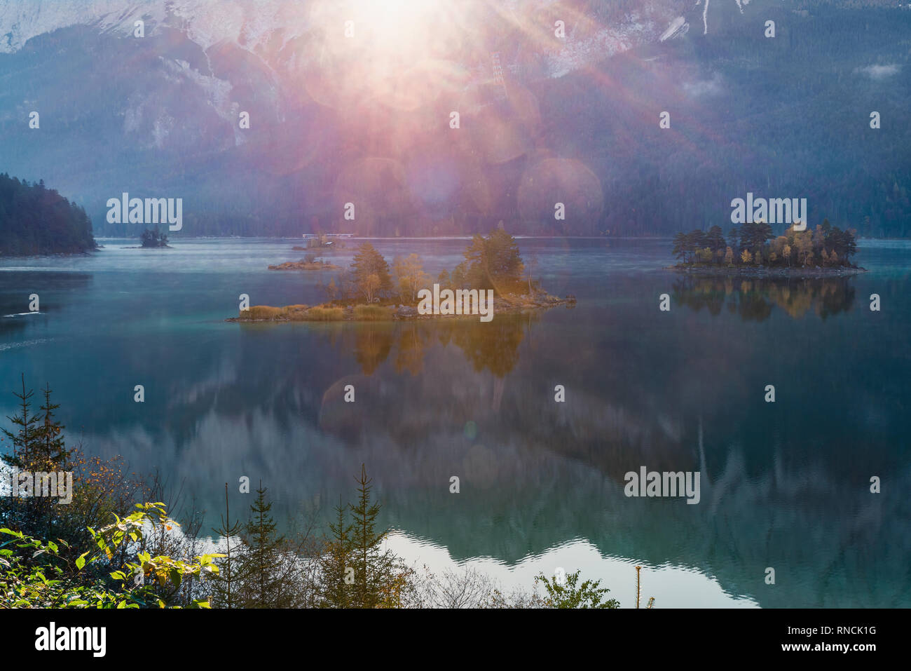 Primi raggi del sole sulla montagna lago Eibsee nelle Alpi Bavaresi. alba sulle montagne e la piccola isola con la riflessione, Germania, Europa Foto Stock