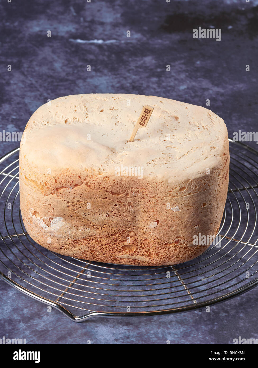 Pane appena sfornato il pane senza glutine, fatta in casa con la macchina per il pane, impostato su una griglia di raffreddamento su sfondo blu scuro Foto Stock