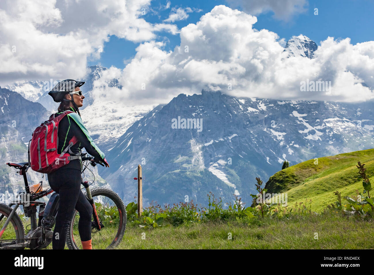 Bella e sempre giovane donna Senior in sella il suo e-mountainbike al di sotto dell'Eiger Northface vicino a Grindelwald e Wengen, Jungfrauregion, Svizzera Foto Stock