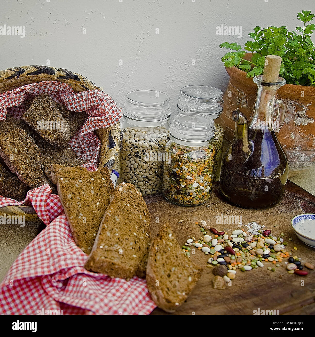 Cesto di pane di segale accompagnato con secchi i fagioli crudi, olio d'oliva su una superficie di legno. Vaso di Ceramica con coriandolo in background. Immagine di stock. Foto Stock