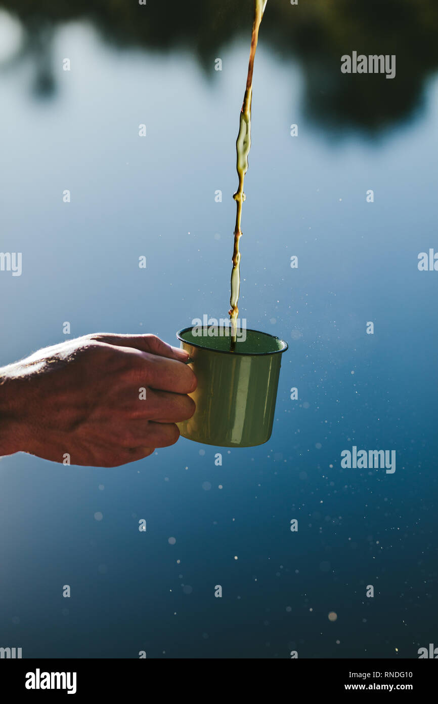 Immagine ravvicinata di una mano che tiene una tazza di tè versando in essa. Il tè che viene versato in una tazza detenuto da una persona all'esterno. Foto Stock