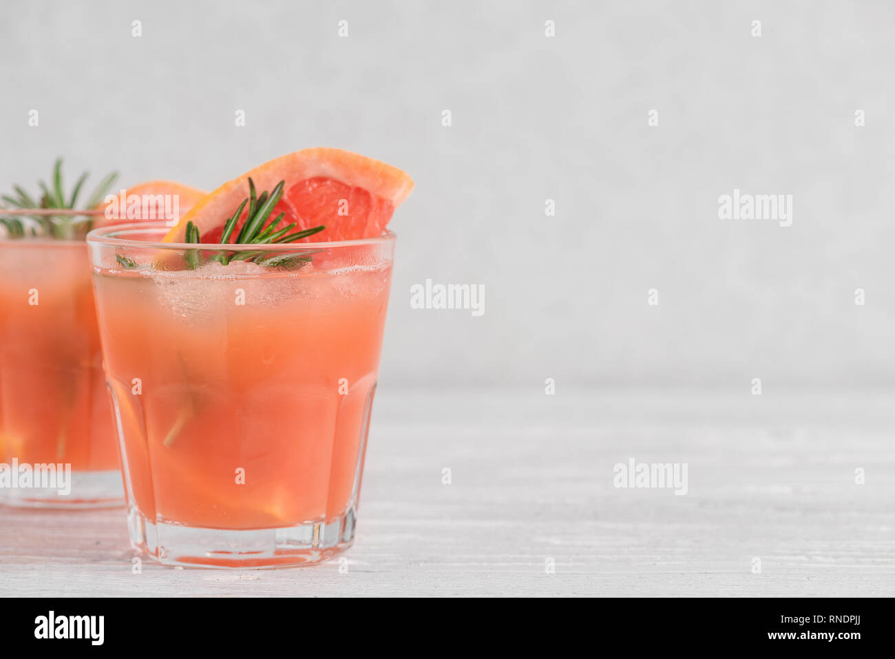 Due bicchieri di succo di pompelmo fresco estate cocktail di alcool, ghiaccio e rosmarino su sfondo bianco. close up Foto Stock