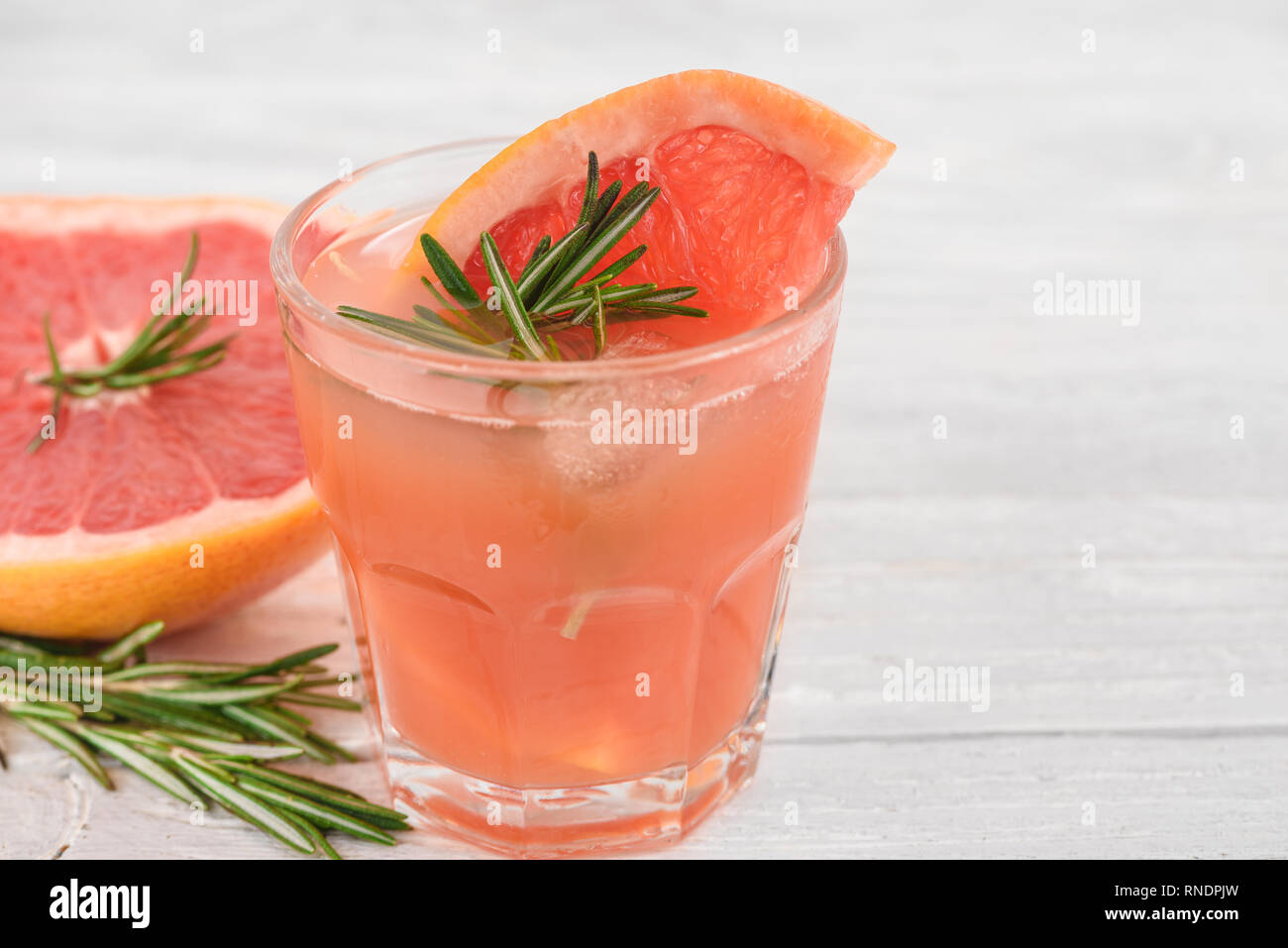 Vetro con succo di pompelmo fresco estate cocktail di alcool, ghiaccio e rosmarino su sfondo bianco. close up Foto Stock