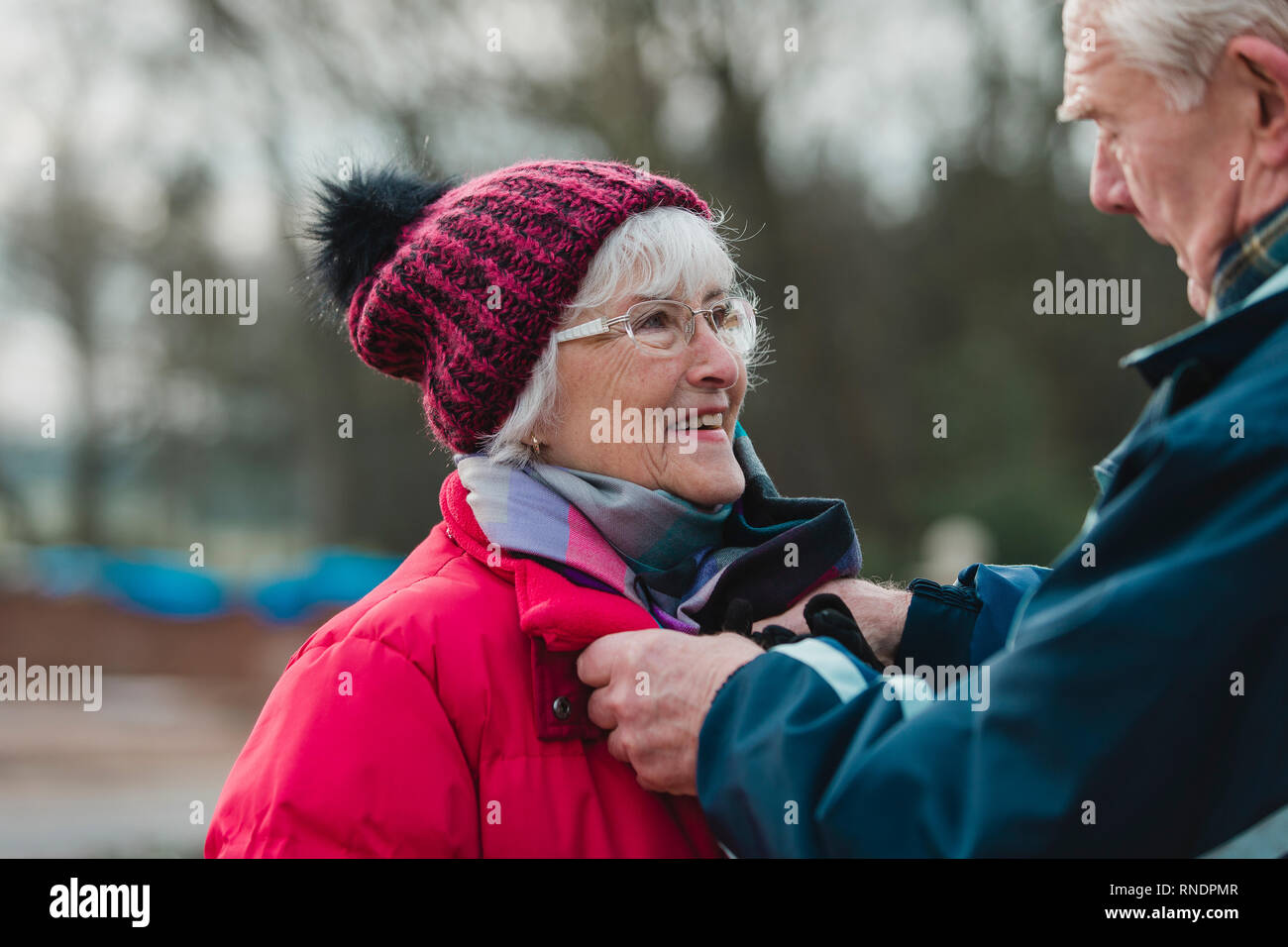 Senior l uomo è messa una sciarpa sulla sua moglie nel loro cortile anteriore prima di lei lascia andare fuori al freddo. Foto Stock