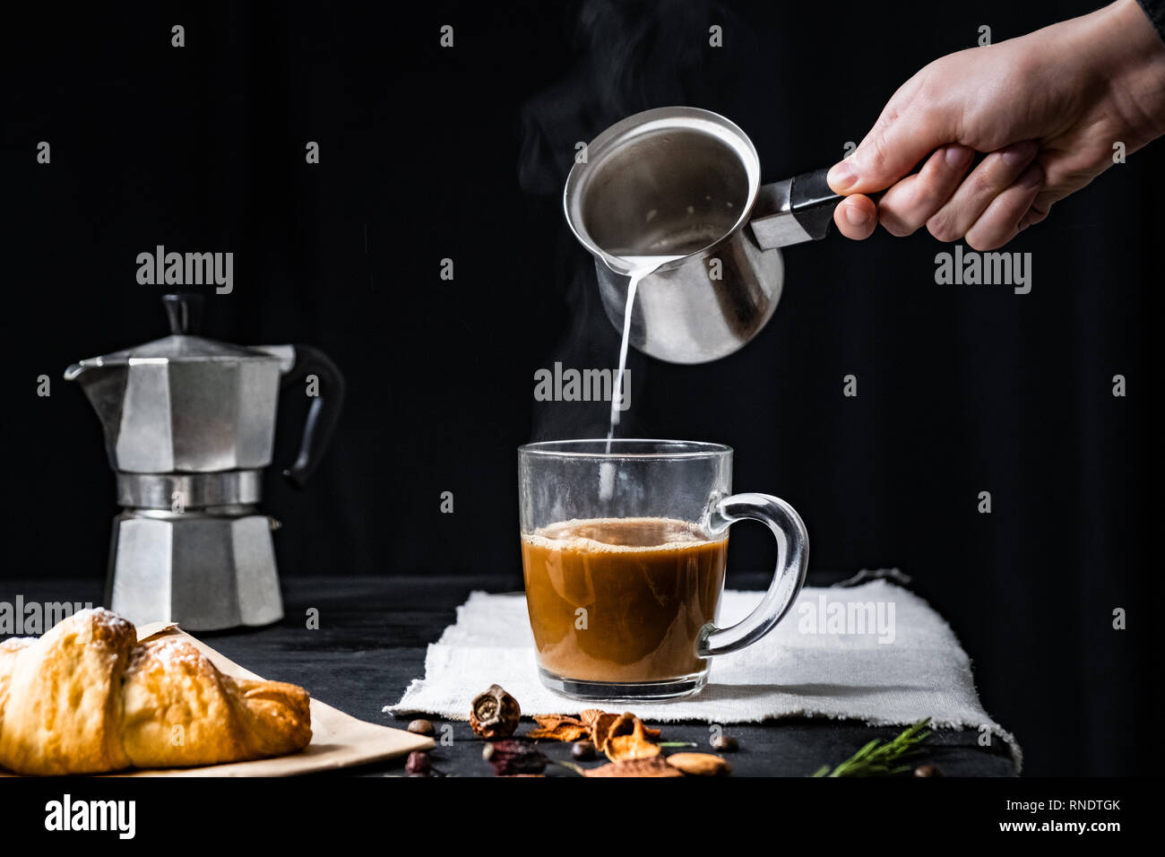 Cottura versare il latte in una tazza di caffè. Aggiunta di latte caldo in caffè espresso prodotta in italiano moka, basso-chiave shot Foto Stock