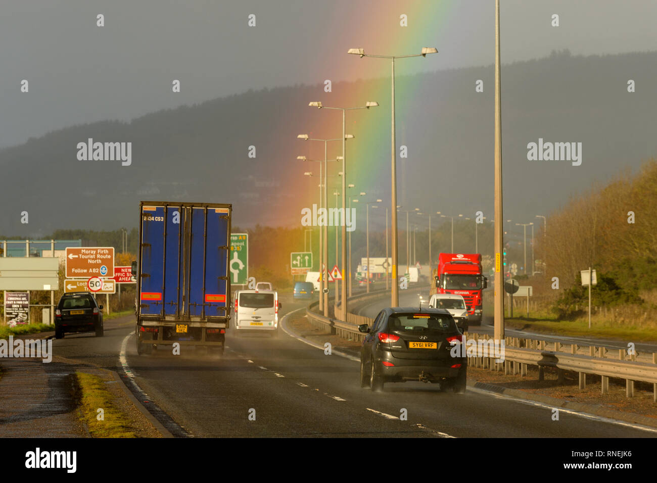 L'A9 trunk road avvicinando il Longman rotonda, Inverness, occupato con il traffico, con un arcobaleno chiaramente visibile. Foto Stock