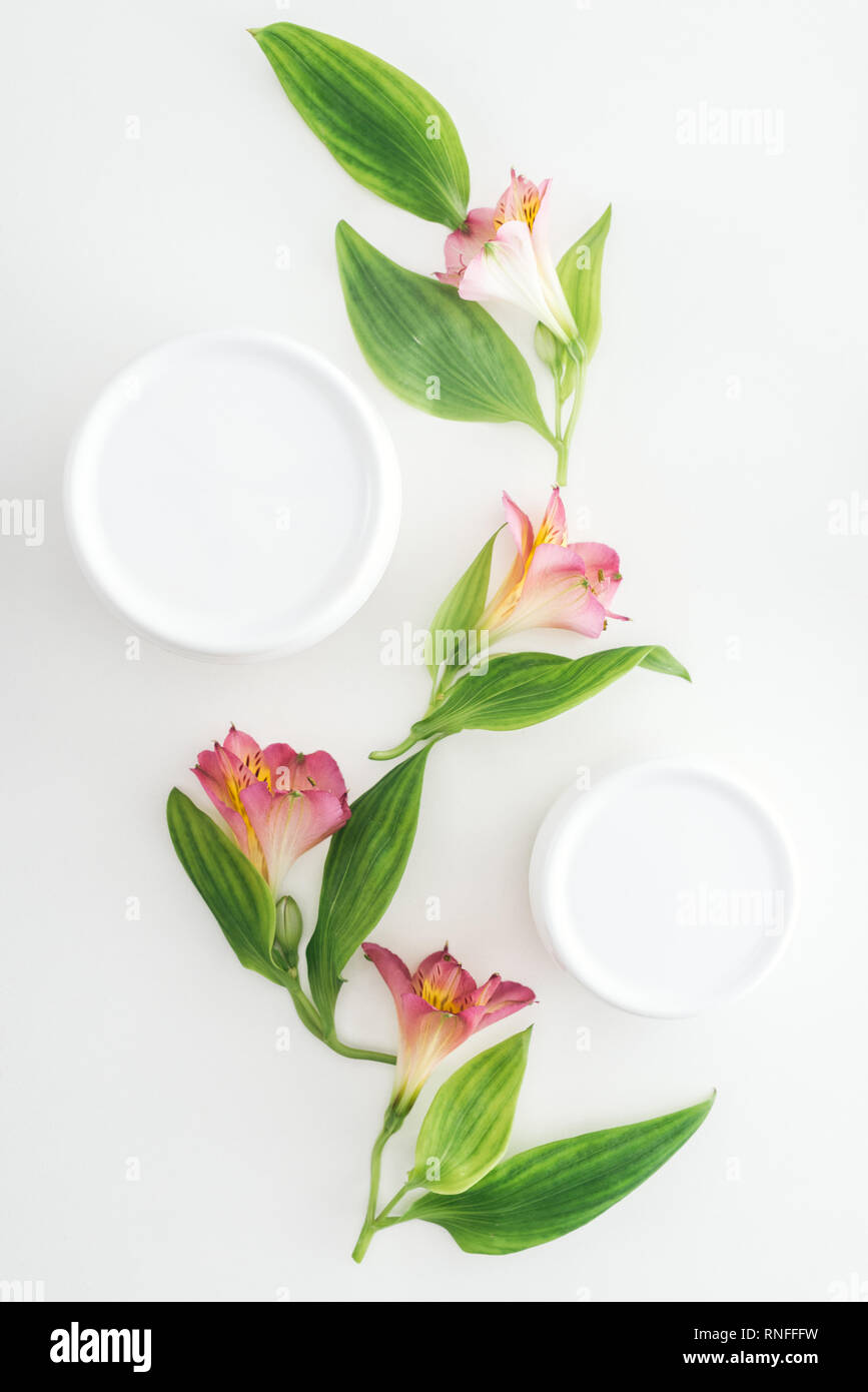 Vista superiore della composizione con alstroemeria rosa fiori, foglie verdi e crema di bellezza in bottiglie su sfondo bianco Foto Stock
