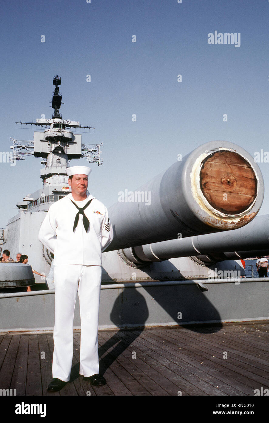 Un crewman in un abito bianco uniforme si erge nei pressi di Mark 7 16 pollici/50-fucili calibro sul ponte di prua della nave da guerra USS NEW JERSEY (BB-62). La nave è stata recentemente qui trainato per il riattacco e la riattivazione. Foto Stock