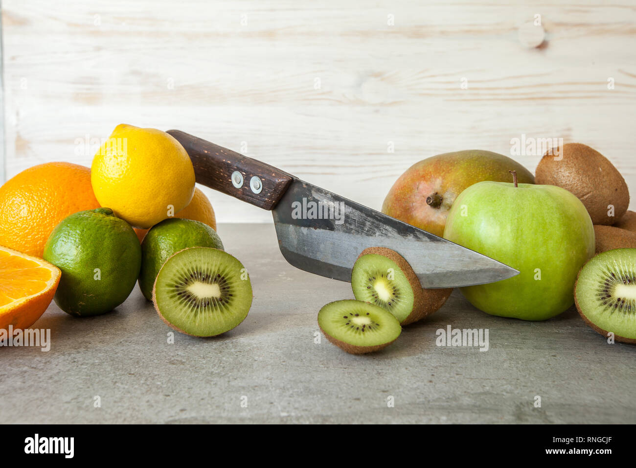 Agrumi freschi, half cut kiwi arancio e limoni sul tagliere con coltello sullo sfondo di pietra. Foto Stock