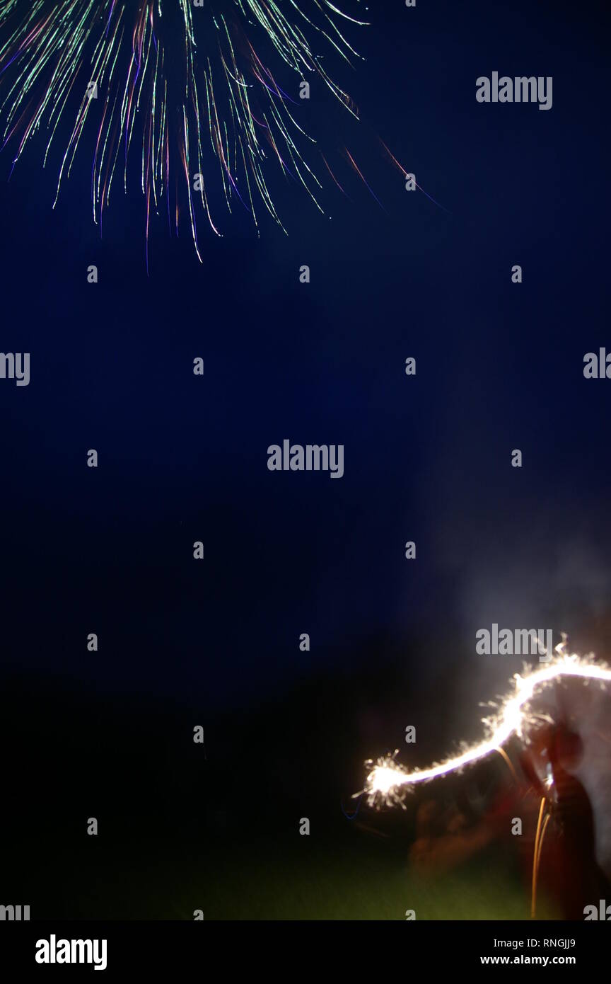 Silhouette di un bambino con la masterizzazione sparkler di notte nell'angolo inferiore destro, fuochi d'artificio che esplodevano in angolo superiore sinistro. Quarto di luglio e per noi il giorno di indipendenza Foto Stock