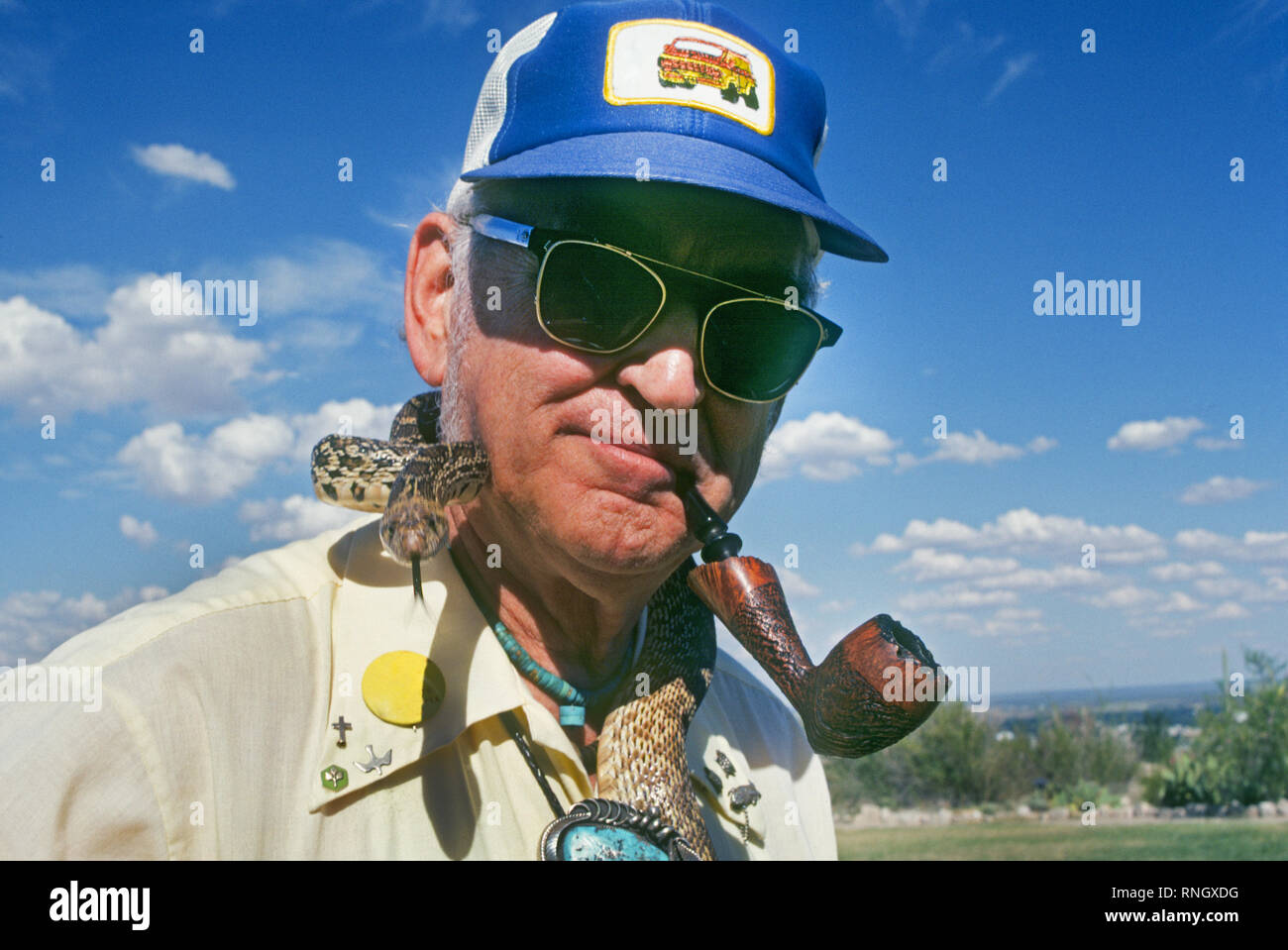Un uomo di fumare un tubo di legno in New Mexico con un western gopher snake avvolto intorno al suo collo Foto Stock
