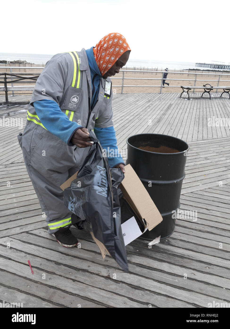 Uomo che lavora per i parchi di New York opportunità programma raccoglie Immondizia sulla Coney Island boardwalk in Brooklyn, New York. Foto Stock Uomo che lavora per i parchi di New York opportunità programma raccoglie Immondizia sulla Coney Island boardwalk in Brooklyn, New York. Foto Stock