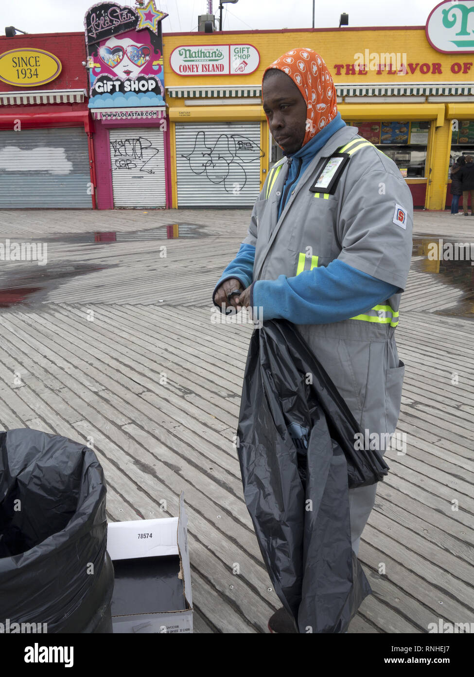 Uomo che lavora per i parchi di New York opportunità programma raccoglie Immondizia sulla Coney Island boardwalk in Brooklyn, New York. Foto Stock Uomo che lavora per i parchi di New York opportunità programma raccoglie Immondizia sulla Coney Island boardwalk in Brooklyn, New York. Foto Stock