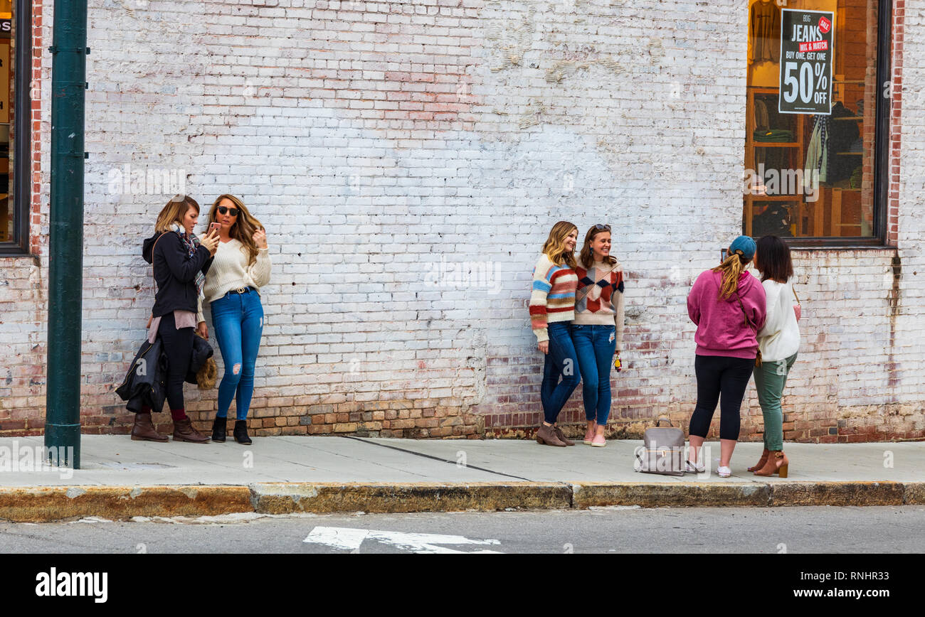 ASHEVILLE, NC, Stati Uniti d'America-2/16/19: giovani donne a turno che posano per una improvvisata smart phone foto, con il bianco muro di mattoni come sfondo. Foto Stock