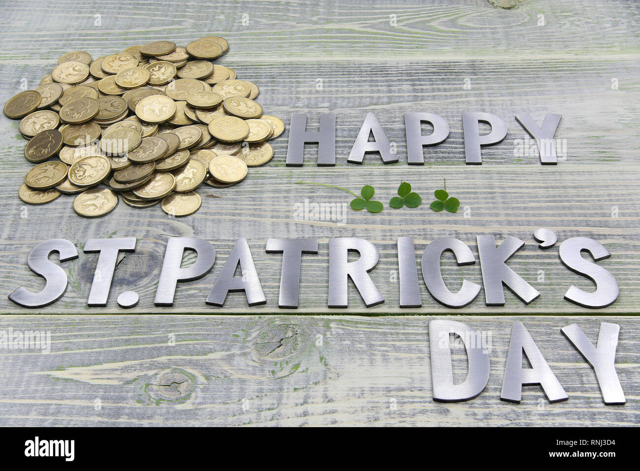 Iscrizione felice Patricks giorno un sacco di oro British monete e tre fogli di trifoglio, giacciono su una superficie strutturata di legno Foto Stock