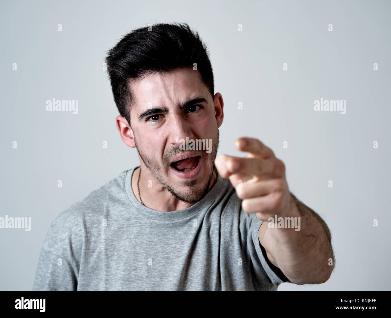 Close up ritratto di Giovane uomo violento con volto arrabbiato cercando furioso e pazzo che mostra si inserisce e puntare il dito verso la telecamera. Viso umano expressi Foto Stock