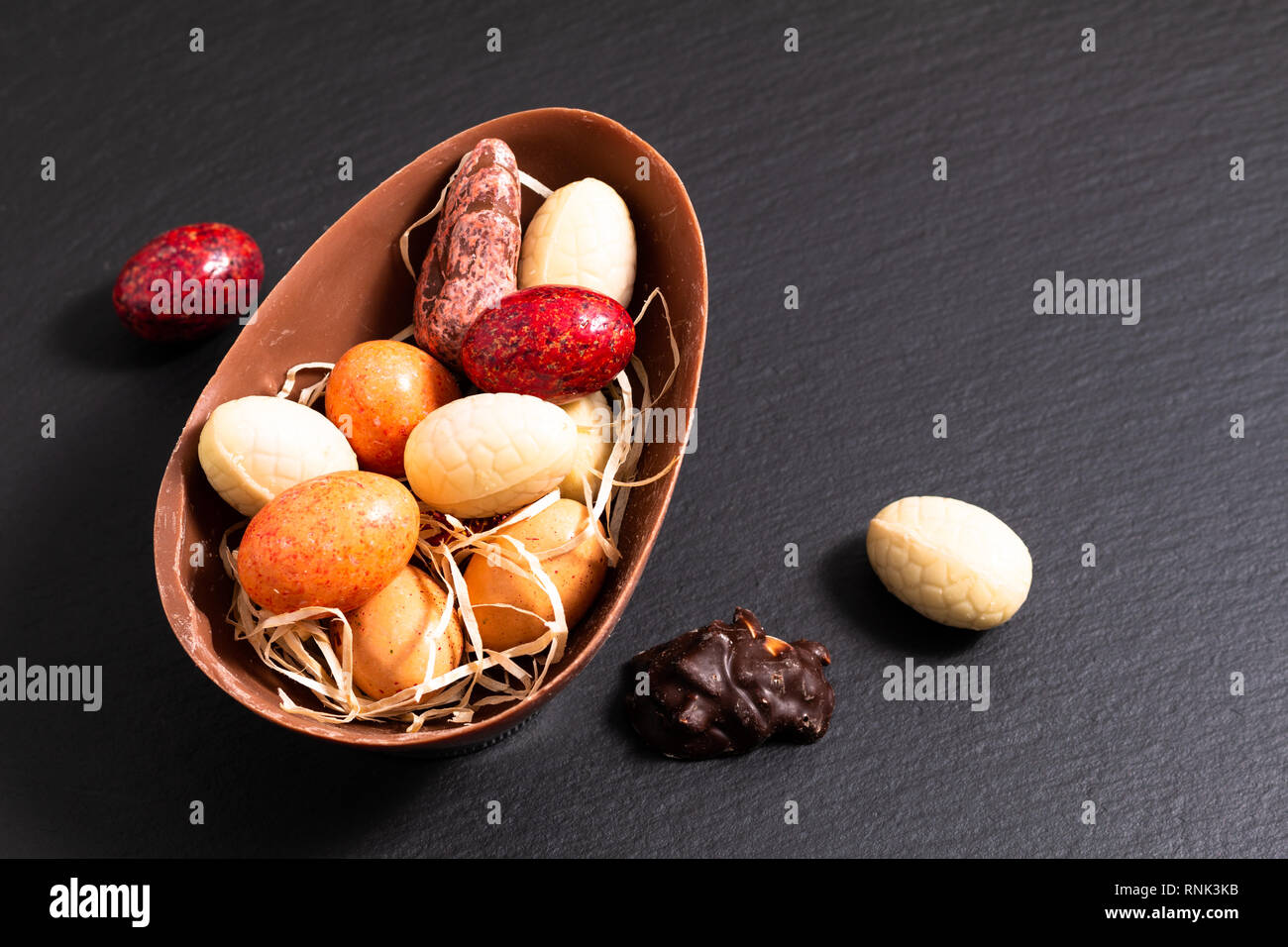 Vacanze concetto alimentare caramelle colorate e uova di pasqua di cioccolato nero sulla piastra di ardesia con spazio di copia Foto Stock