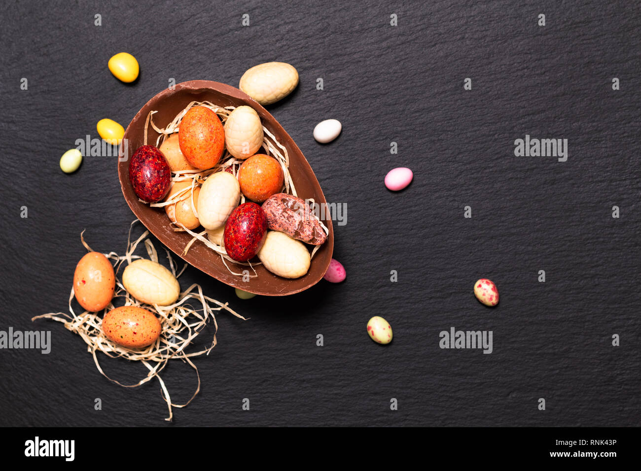 Vacanze concetto alimentare caramelle colorate e uova di pasqua di cioccolato nero sulla piastra di ardesia con spazio di copia Foto Stock