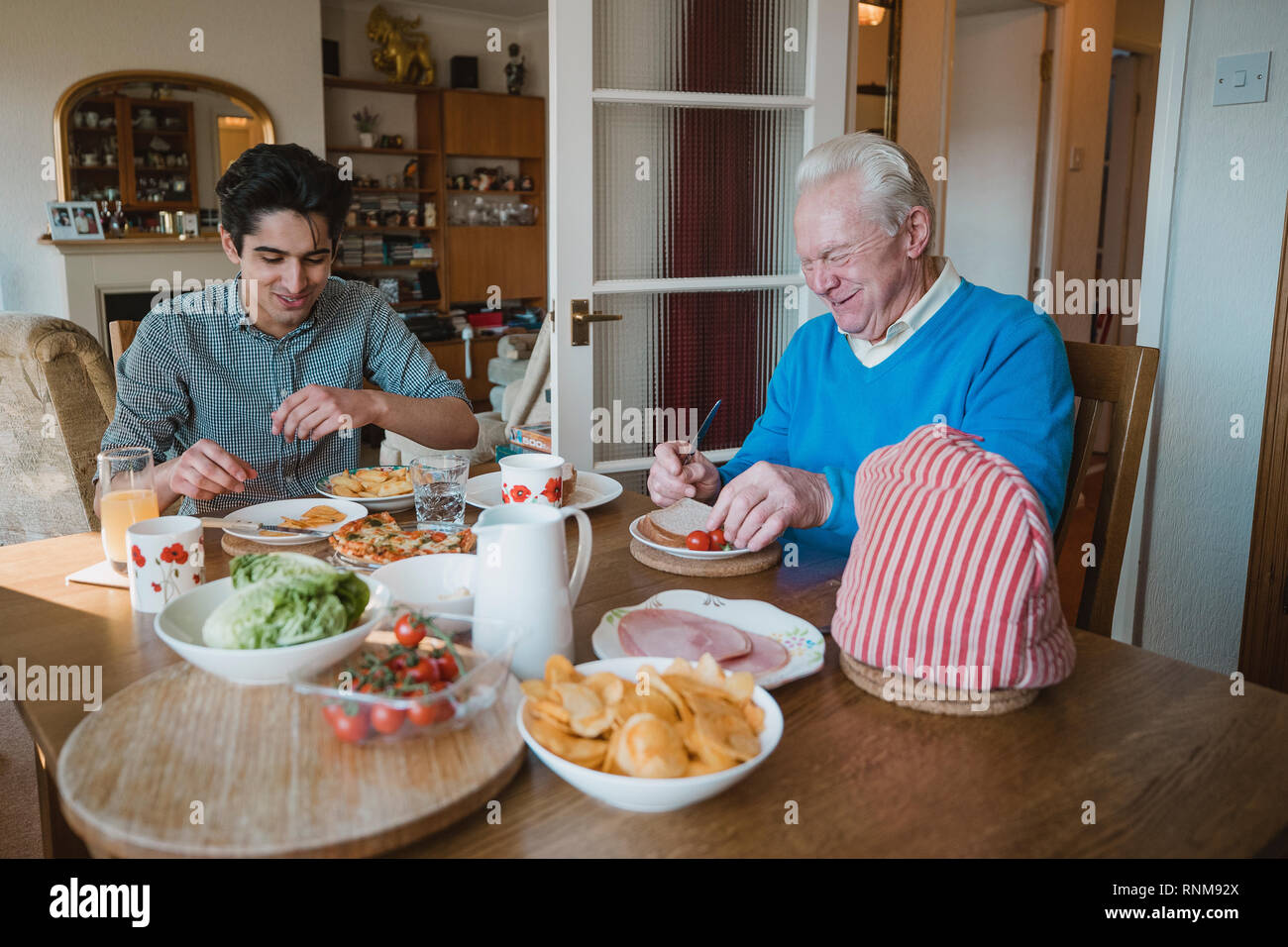 L'uomo anziano è a pranzo a casa con il suo nipote. Essi stanno mangiando panini, pizza e patatine. Foto Stock