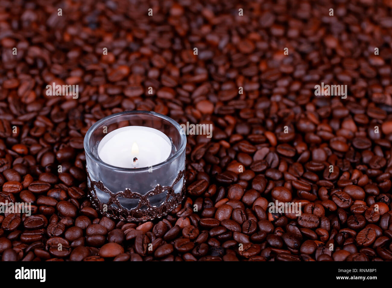 Un mucchio di chicchi di caffè tostati e una vecchia candela accesa. Foto Stock