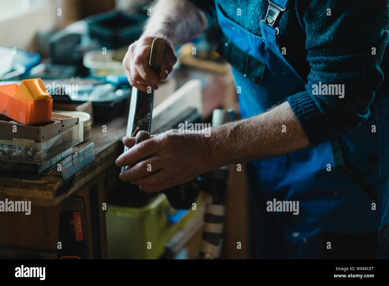 Immagine ravvicinata di un uomo anziano con una pialla surform su legno nella sua bottega. Foto Stock
