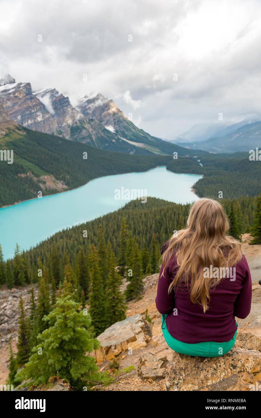 Giovane donna seduta su una pietra cercando in natura, turchese, Lago Peyto Lake, Montagne Rocciose, il Parco Nazionale di Banff, provincia di Alberta, Canada, Nord Foto Stock