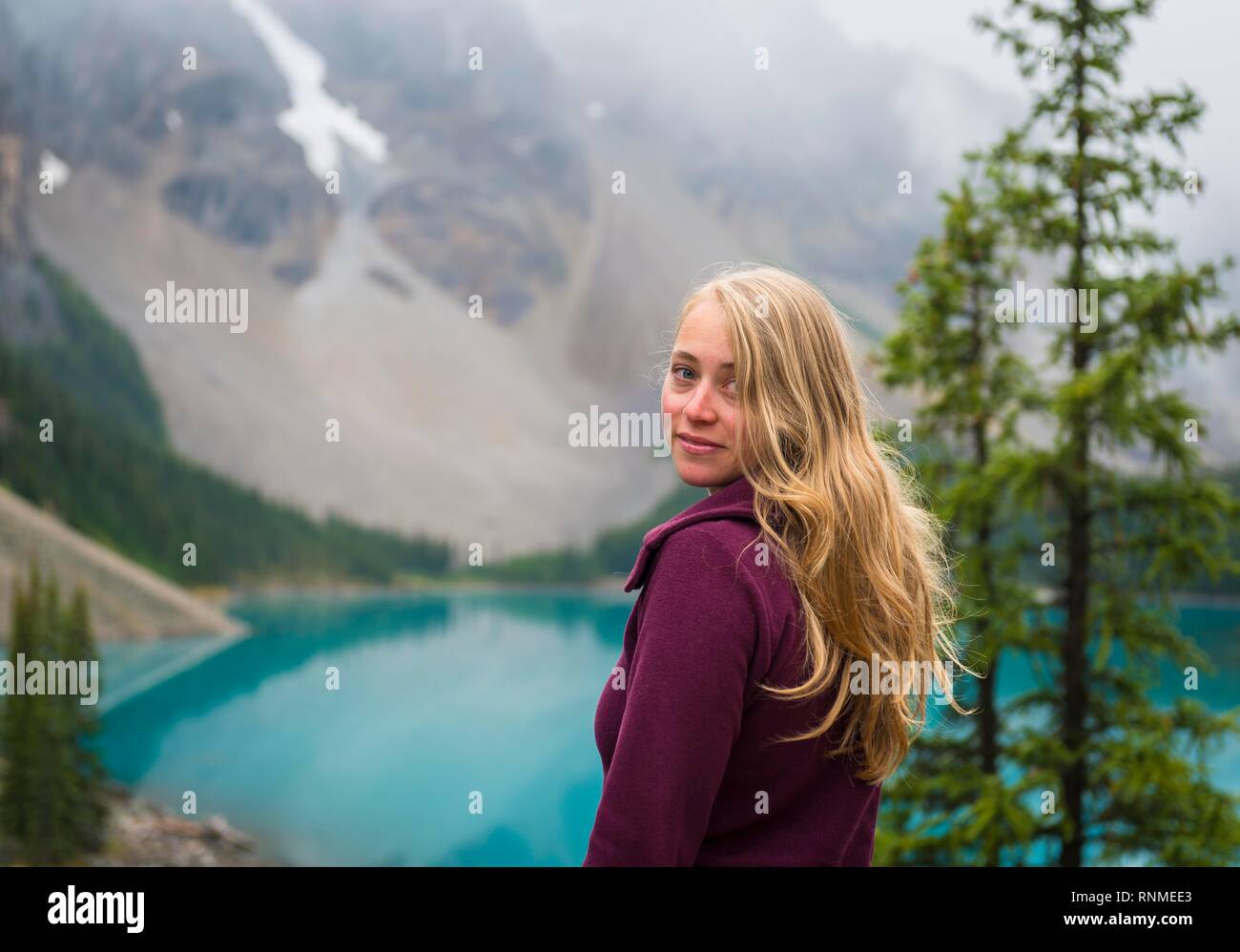 Giovane donna guarda nella telecamera, il Lago Moraine, Valle dei Dieci Picchi, Montagne Rocciose, il Parco Nazionale di Banff, provincia di Alberta, Canada, Nord Americ Foto Stock